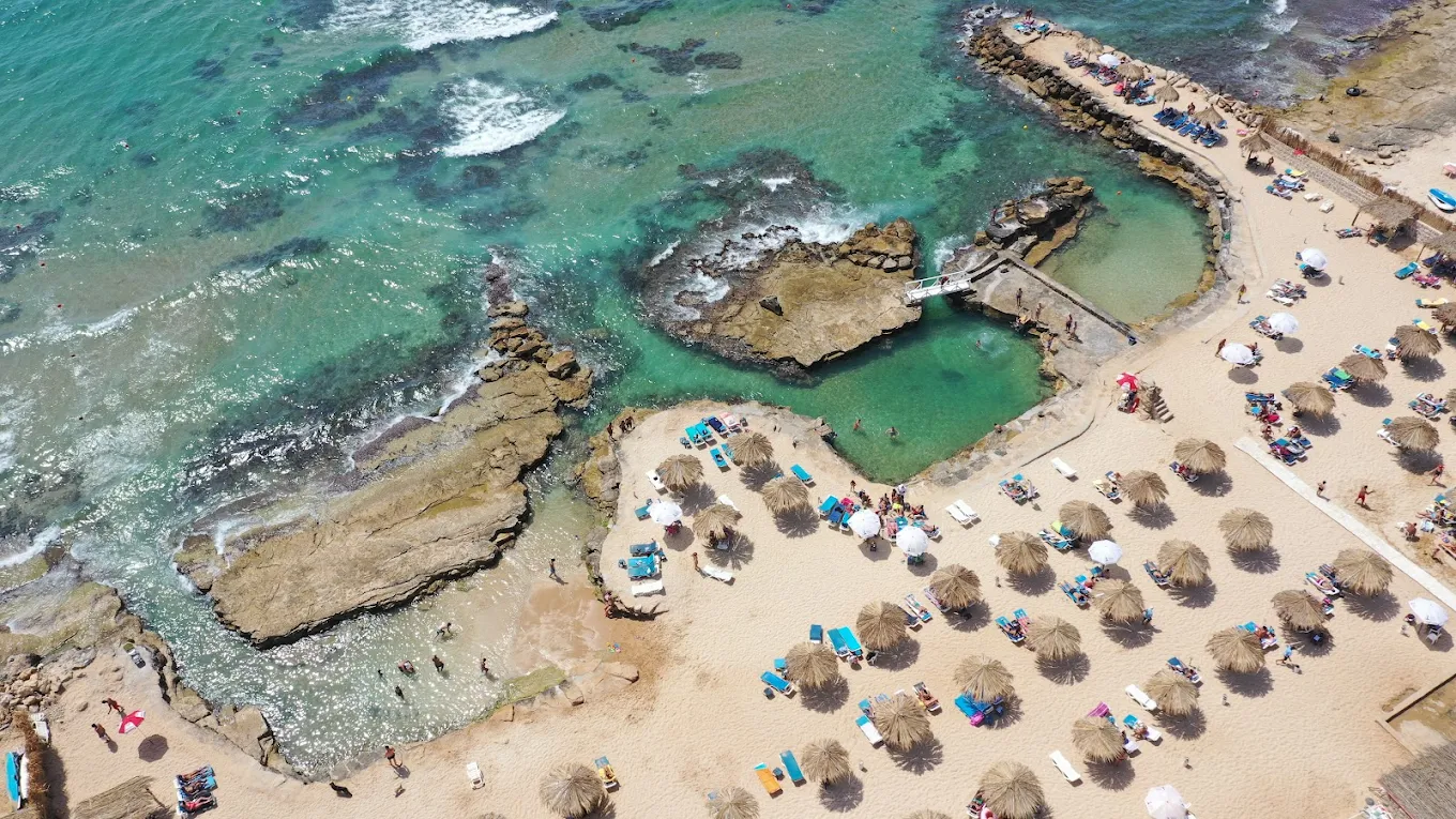 Aerial view of Side B beach with thatched umbrellas and rock pools
